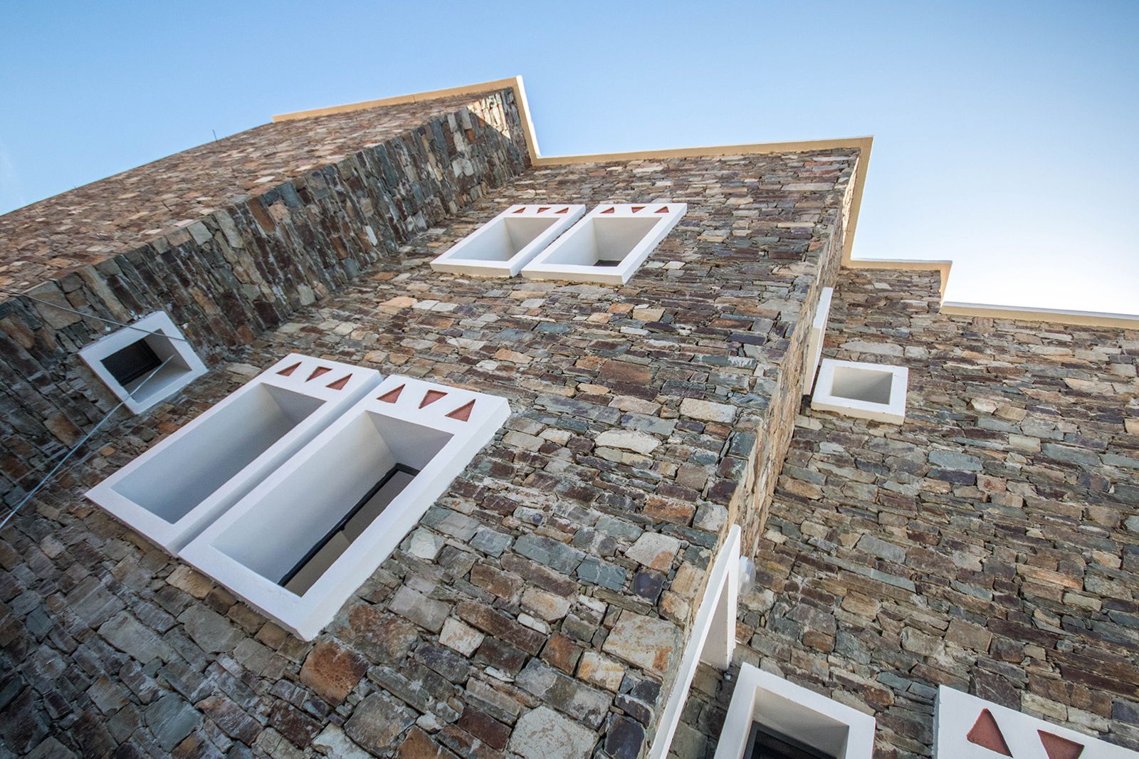 Façade en pierre en contre-plongée, fenêtres blanches à motifs triangulaires