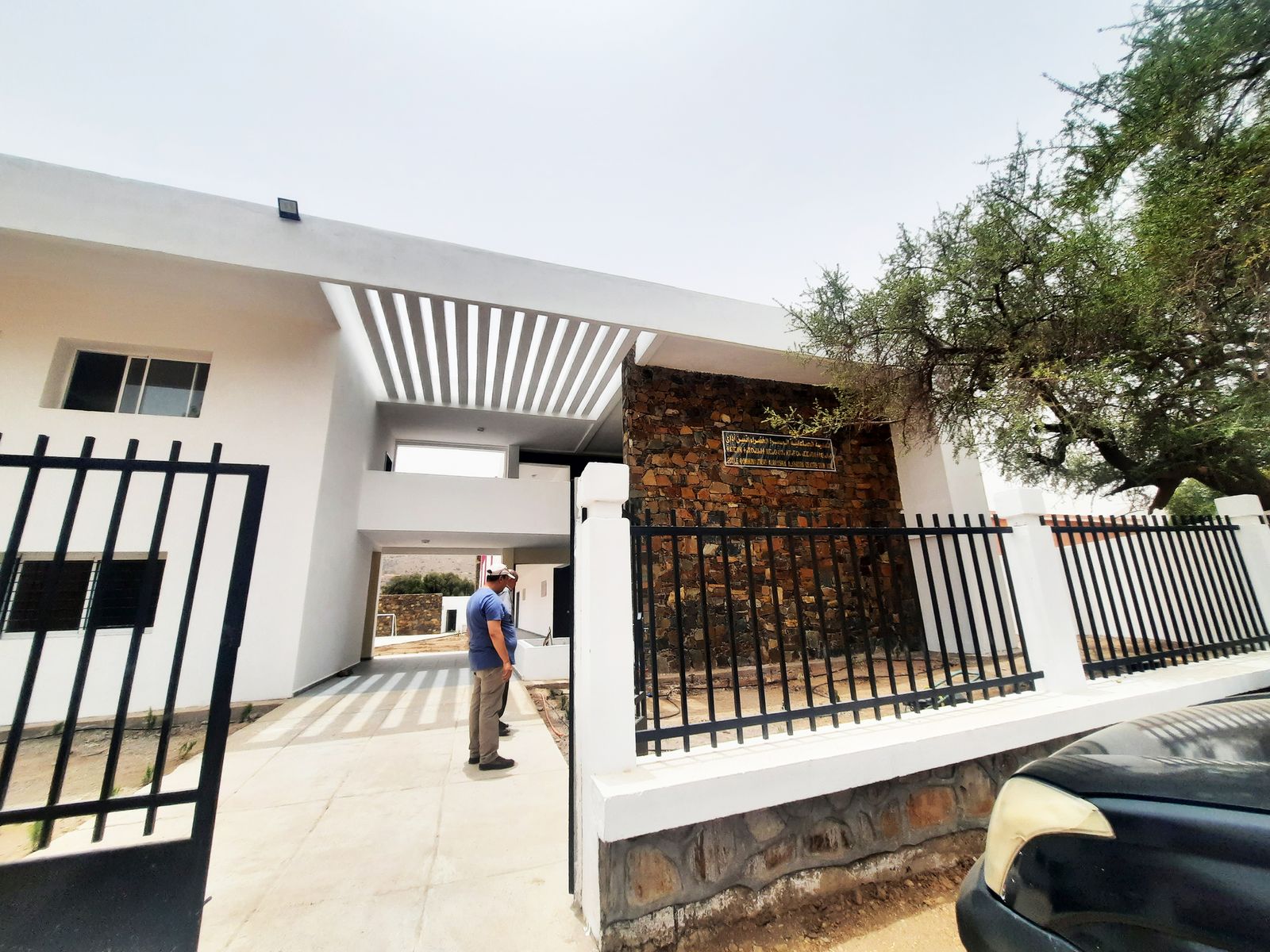 Entrée de l'école communautaire, pergola blanche et mur en pierre