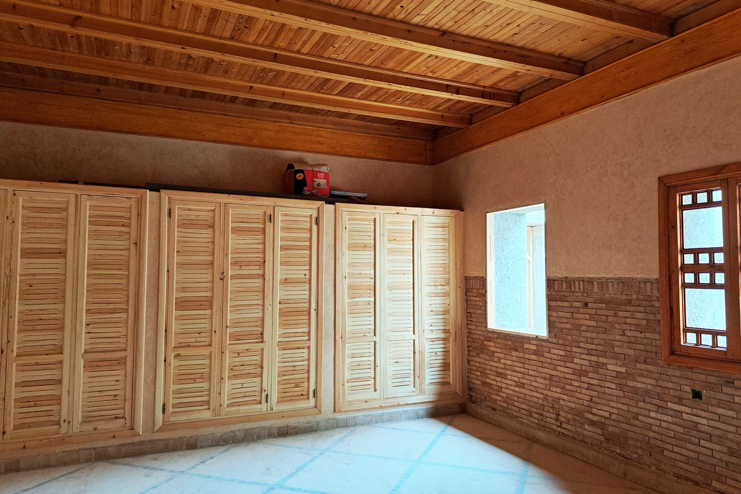 Chambre avec plafond en bois, placards à persiennes et soubassement en brique