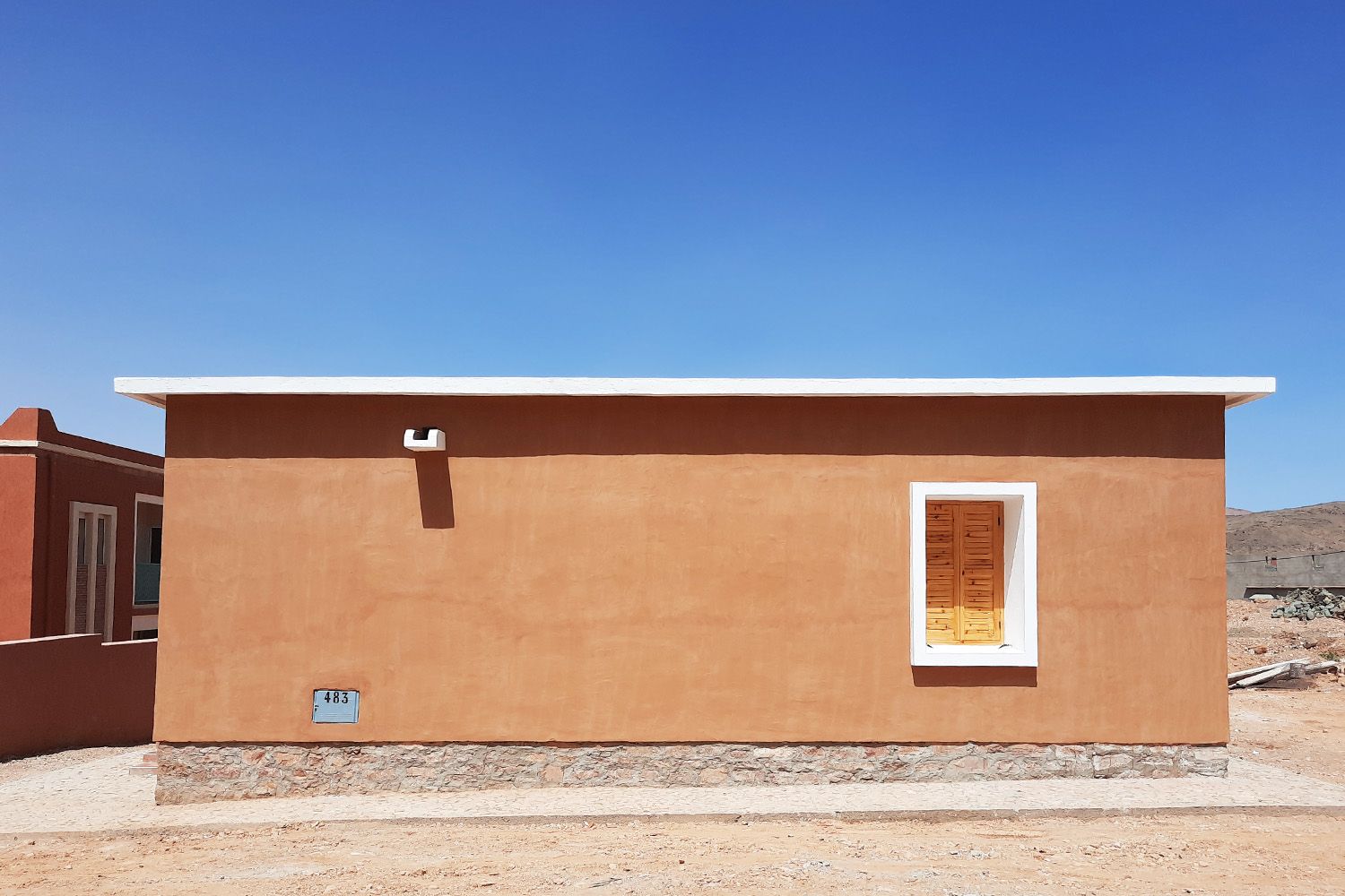 Logement en pisé enduit sur soubassement en pierre, sous un ciel bleu